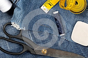 Torn blue denim cotton fabric trousers with tailor`s tools - jeans fashion mending or repair concept, flat lay top view