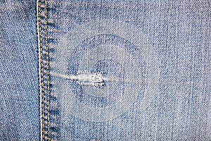 Torn blue jeans with a hole and seam with stitches close up