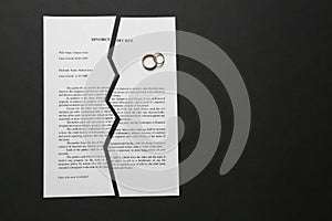 Torn divorce decree with rings on dark background