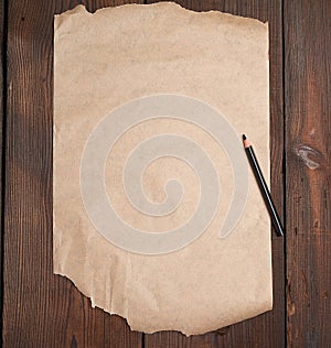 Torn empty sheet of brown paper and a black pencil on a wooden surface