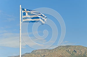 Torn greek flag on flag-post against blue sky