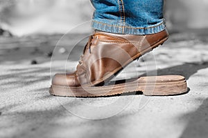 Torn men`s shoes in the street. Torn shoe on foot. Footwear requiring repair.