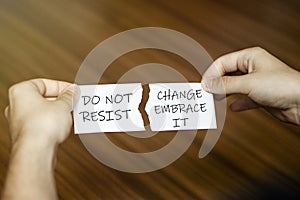 Torn paper with text Do Not Resist Change Embrace It in male hands on wood background