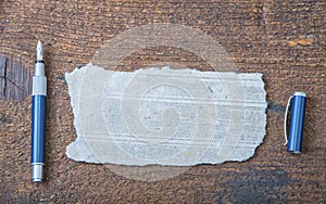 Torn piece of old paper for message or word of wisdom with pen on brown wood