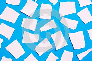 Torn pieces of white blank paper laid out randomly on a blue cardboard background