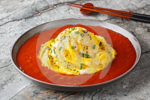 Tornado omelette on top of fried rice with sesame seeds, green onions and hot pepper sauce close-up in a plate. Horizontal