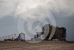 A tornado reaches down from a storm cloud behind a farm in the rural countryside.