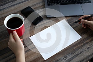 Toronto, Canada - 30, April, 2020: Hands writing on blank paper with copy space with coffee cup, phone, laptop on wooden desk tabl