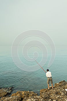 A local fisherman casting his fishing rod into the Mediterranean sea on the rocks off the coast of Torrox