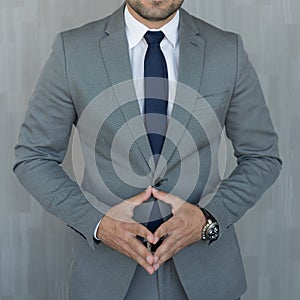 Torso of anonymous businessman standing with hands in lowered steeple wearing beautiful fashionable classic grey suit