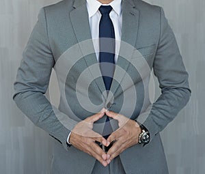 Torso of anonymous businessman standing with hands in lowered steeple wearing beautiful fashionable classic grey suit