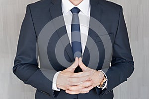 Torso of anonymous businessman standing with hands in lowered steeple, wearing beautiful fashionable classic navy blue