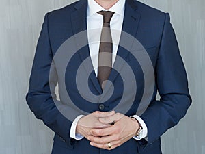 Torso of a businessman standing with hands clenched in middle position in a classic navy blue suit.