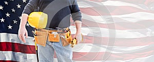 Torso of a Male Contractor Wearing Tool Belt Holding Blank Yellow Hardhat and Gloves Over Waving American Flag Background Banner