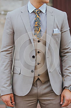 The torso of a man in a light gray suit and beige shirt with blue and yellow paisley tie