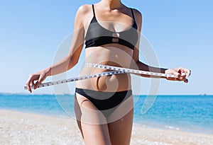 Torso of woman in bikini with tape-measure on beach
