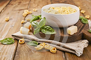 Tortellini mignon on a wooden board with basil and parmesan. Specialties of the cuisine from Bologna and Emilia Romagna