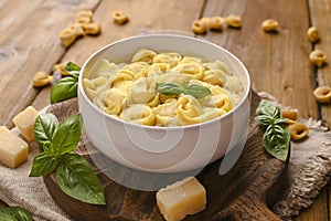 Tortellini mignon on a wooden board with basil and parmesan. Specialties of the cuisine from Bologna and Emilia Romagna