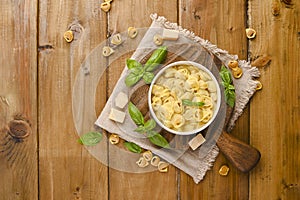 Tortellini mignon on a wooden board with basil and parmesan. Specialties of the cuisine from Bologna and Emilia Romagna