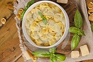 Tortellini mignon on a wooden board with basil and parmesan. Specialties of the cuisine from Bologna and Emilia Romagna