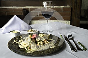 Tortellini pasta with white sauce served on a marble plate with a glass of wine and cuttery.