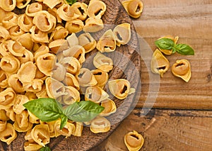 Tortellini on a wooden board with basil and parmesan. Specialties of the cuisine from Bologna and Emilia Romagna
