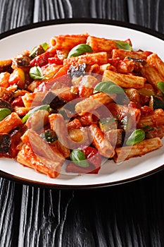 Tortiglioni pasta with eggplant, zucchini, pepper and basil in tomato sauce close-up in a plate. vertical