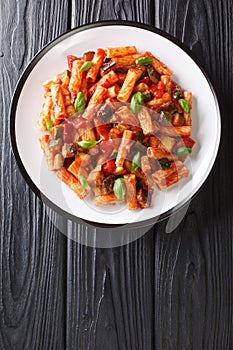 Tortiglioni pasta with eggplant, zucchini, pepper and basil in tomato sauce close-up in a plate. Vertical top view