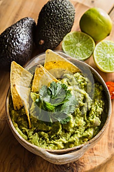 Tortilla chips in bowl of guacamole with avocado and limes