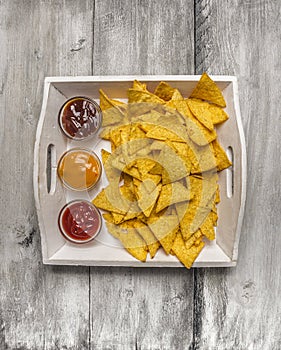 Tortilla chips with cheese, tomato and barbecue dips on white wooden background. Snack food