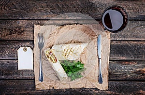 Tortilla wrap with chicken breast and vegetables. Served by cutlery and fresh lemonade on a wooden background.