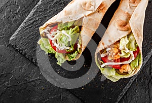Tortilla wraps with grilled chicken, fresh vegetables and salad on black stone background. Healthy snack or take-away lunch.