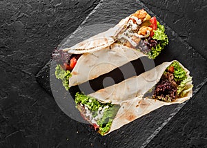 Tortilla wraps with grilled meat, fresh vegetables and salad on black stone background. Healthy snack or take-away lunch. Top view