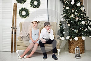 The tortured brother and sister are sitting on the couch by the Christmas tree photo
