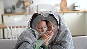 Tortured European mother and daughter suffer from cold and wrapped in blanket sits on sofa