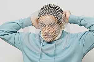 tortured, suffering from problems, a man with a mesh on his face stands in a light blue hoodie on a light background and