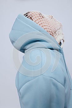 tortured, suffering from problems, a man with a mesh on his face stands in a light blue hoodie on a light background