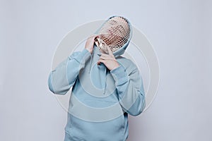 tortured, suffering from problems, a man with a mesh on his face stands in a light blue hoodie on a light background and