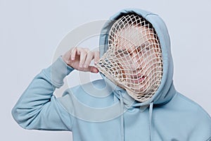 tortured, suffering from problems, a man with a mesh on his face stands in a light blue hoodie on a light background and