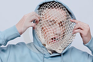 tortured, suffering from problems, a man with a mesh on his face stands in a light blue hoodie on a light background and