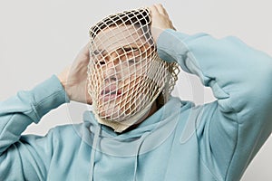 tortured, suffering from problems, a man with a mesh on his face stands in a light blue hoodie on a light background and