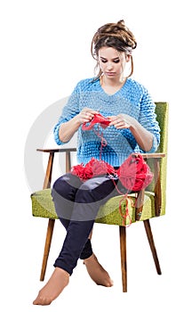 Tortured young girl in a sweater sits on a chair with a red ball of yarn and knitting a scarf and Spitz. Tired. White background. photo