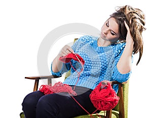 Tortured young girl in a sweater sits on a chair with a red ball of yarn and knitting a scarf and Spitz. Tired. White background.