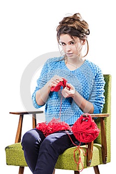 Tortured young girl in a sweater sits on a chair with a red ball of yarn and knitting a scarf and Spitz. Tired. White background.