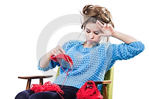 Tortured young girl in a sweater sits on a chair with a red ball of yarn and knitting a scarf and Spitz. Tired. White background. photo