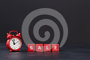 Total sale. Red cubes with one white, alarm clock on dark background, copy space. Time to sale. Black friday. Sell-out.