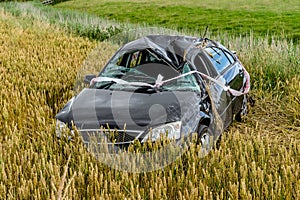Totaled, black wrecked car after rollover in field,