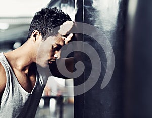 Totally exhausted....A muscular young man leaning against a boxing bag and looking defeated.