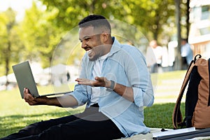 Always in touch concept. Excited african american man using laptop outdoors and making video call, resting in city park