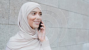 Always in touch. Peaceful young middle eastern woman wearing traditional headscarf talking on cellphone outdoors
